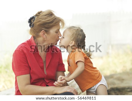 Grandma kisses granddaughter. They sit under the open sky on a summer day.