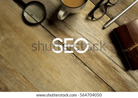 Top view of magnifier, a cup of coffee, eye glasses,  pen and notebook written with SEO (SEARCH ENGINE OPTIMIZATION) on wooden background. A business concept.