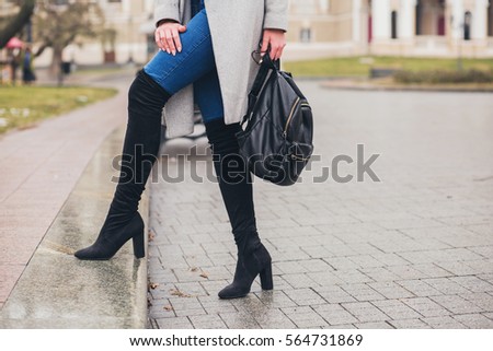 young stylish woman walking in autumn city, cold season, wearing high heeled black boots, leather backpack, accessories, grey coat, fashion trend, legs close-up details