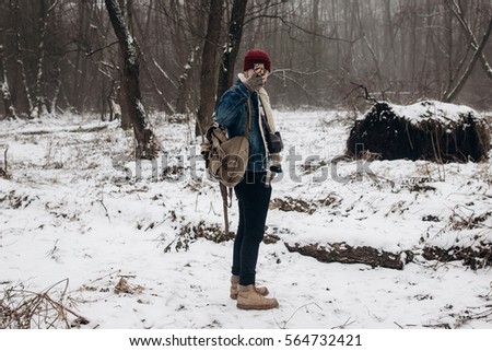 stylish hipster traveler with backpack holding smartphone and taking picture in winter snowy forest. wanderlust and adventure concept with space for text. atmospheric moment