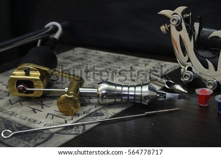 Tattoo machine with ink and sketches on tattoo skins on dark wooden background