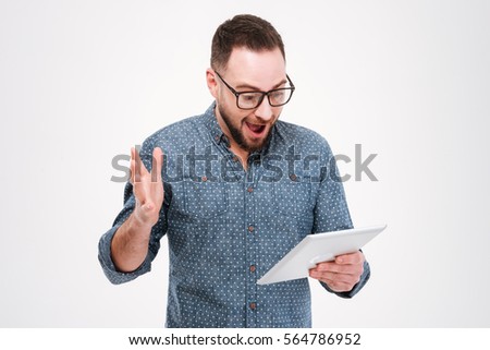 Image of cheerful shocked bearded man wearing glasses dressed in blue shirt using tablet computer isolated over white background.
