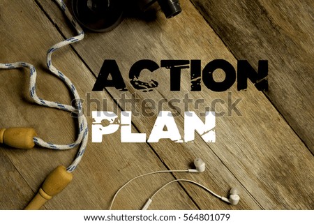 Top view of skipping rope, water bottle and  earphone with ACTION PLAN written on wooden background.  Fitness conceptual.