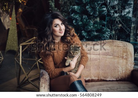 beautiful smiling brunette girl with cat in her hands, sitting on sofa