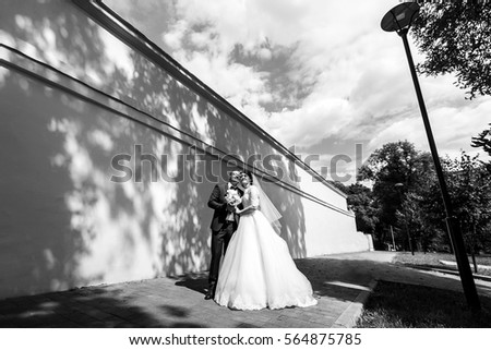 Black and white picture of stunning newlyweds standing in trees' shadows under the sky full of clouds