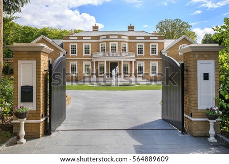 Looking through grand entrance gates to an elegant modern mansion Royalty-Free Stock Photo #564889609