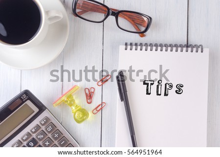  TIPS text on notebook.coffee,calculator,pen,rubber stamp,glasses on the desk.top view.