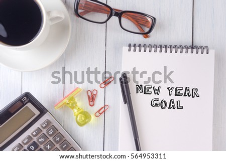 NEW YEAR GOAL text on notebook.coffee,calculator,pen,rubber stamp,glasses on the desk.top view.