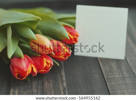 Tulips and an empty white card for the text on a wooden surface. Spring bouquet of flowers, soft focus.