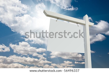 Blank Real Estate Sign over Clouds and Blue Sky with Sun Rays.