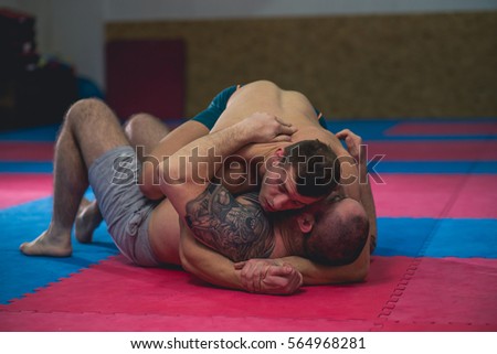 Mixed martial art fighters grapple and wrestle on the ground of a gym