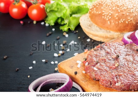 Burger ingredients. Raw meat, onion, pepper, burger on a wooden board on slate, concrete. Hamburger for lunch at home, office, restaurant and place for text on the site.