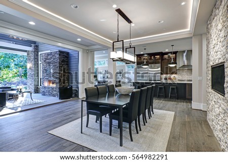 Modern open floor plan dining room design accented with stone fireplace wall facing black dining table with leather chairs overlooking lush outdoors. Northwest, USA