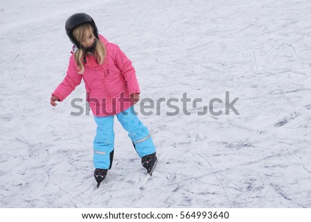 Happy little girl skating in winter outdoors, wearing safety helmet
