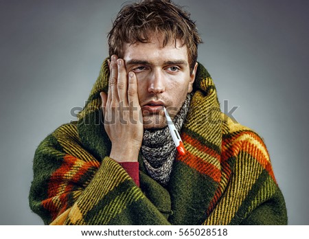 Ill young man with a thermometer in his mouth wrapped in plaid. Healthcare concept Royalty-Free Stock Photo #565028518