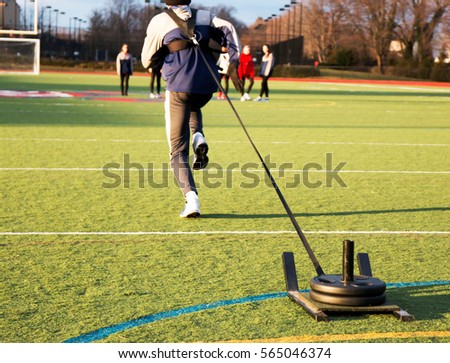 Track and field sprinter pulling a weighted sled on a green turf field during sprinting practice