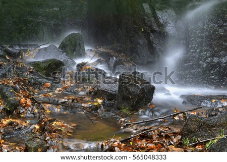 Misty waterfall and rocks in a woodland stream during autumn.