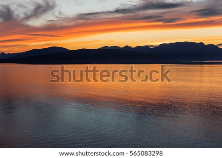 Alaskan coastline sunset with mountain silhouette with ocean of orange reflection