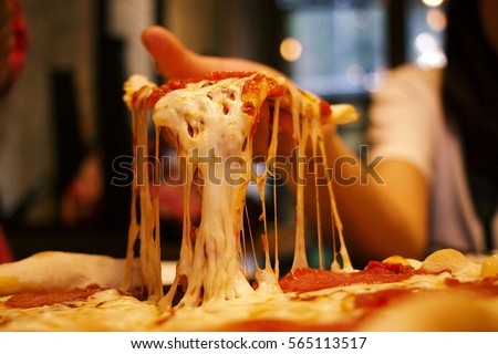 Very cheesy pizza slice in hand.Pizza is a savory dish of Italian origin, consisting of a usually round, flattened base of leavened wheat-based dough topped.