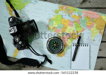 Analog camera, word map, notepad, pen and compass on wooden background