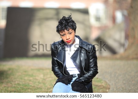 African American black woman touching her hairs, while sitting at street, wearing dark leather jacket and jeans, fashion afro woman, autumn or spring forest outdoors,  close portrait beautiful bokeh