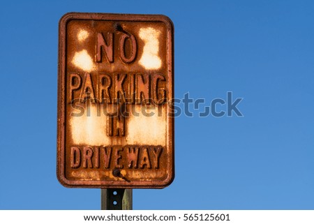 Rusted "No Parking in Driveway" sign with blue sky in background.
