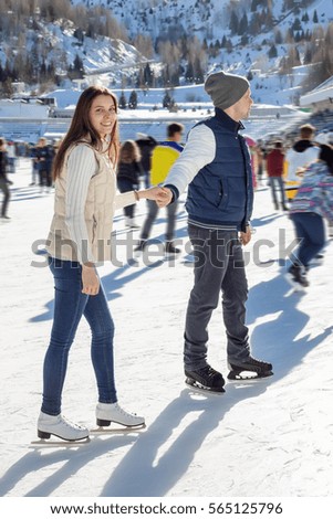 Loving couple skating together holding hands. Mountains in the background