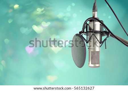 Condenser microphone with pop filter windscreen on stand ready for recording on stage in party event .
Hugh fidelity microphone on stage with colourful heart  bokeh background .