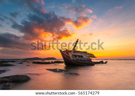 An old shipwreck or abandoned shipwreck.,Boat capsized on a rocky beach in beautiful sunset background Royalty-Free Stock Photo #565174279