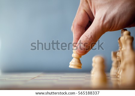 Chess game player makes a move the white pawn one step forward. Chess pieces on the board on blue background. Chessman playing chess and makes the first move a pawn, and showing the hand. 