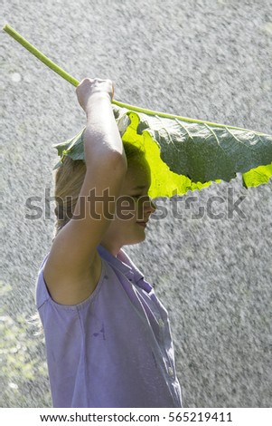 A girl of twelve closed from the rain under the leaves of plants.