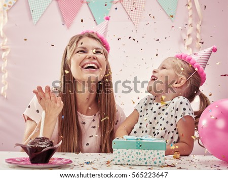 Happy family playing with falling confetti over festive pink background.