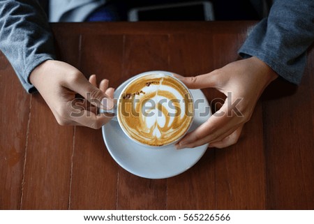 Hot latte art with heart foam picture on surface serve in white cup on the wooden table in woman hands.