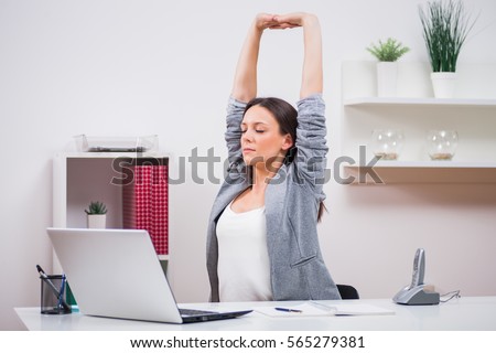 Young businesswoman is relaxing in her office. She is stretching her body. Royalty-Free Stock Photo #565279381