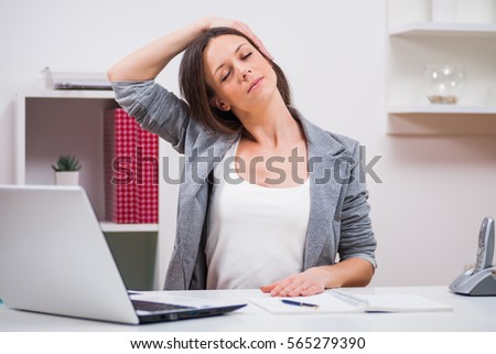 Young businesswoman is relaxing in her office. She is stretching her body. Royalty-Free Stock Photo #565279390