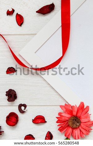 Top view of red dry petal, ribbon, flower and white picture frame for your text for a love Valentine`s day on wooden background. Flat lay.