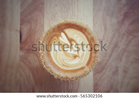 Vintage picture cup of coffee with two hearts milk foam pattern and peanut butter crumble coated cup mouth on wooden background.