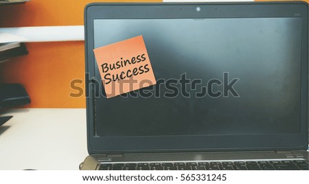 A Technology concept image of a laptop with black screen on an office desk with a red sticky note contain word BUSINESS SUCCESS