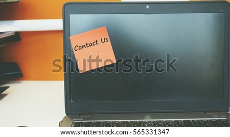 A Technology concept image of a laptop with black screen on an office desk with a red sticky note contain word Contact Us