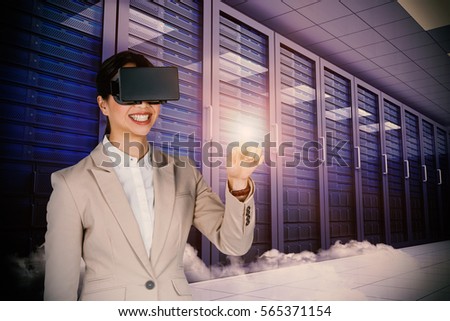 Smiling businesswoman pointing while wearing virtual video glasses against digitally generated server room with towers