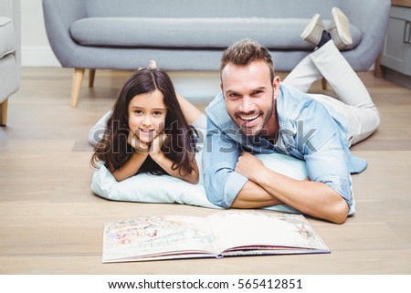 Portrait of father and daughter with picture book lying on floor at home