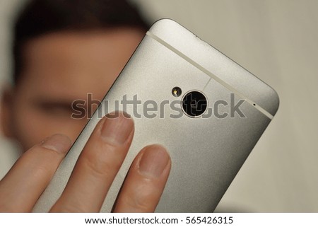 Male hand holding a silver smart cellular phone while taking selfie with a front camera as a symbol of trends of young people and virtual social networking 