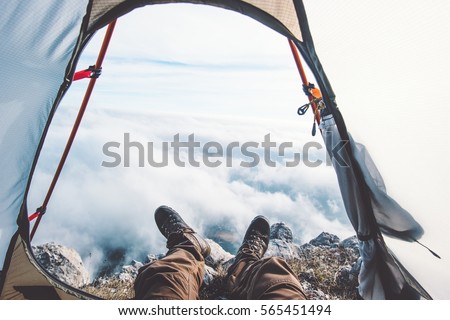 Feet Man relaxing enjoying clouds mountains aerial view from tent camping entrance outdoor Travel Lifestyle concept adventure vacations outdoor Royalty-Free Stock Photo #565451494