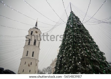 Christmas tree at winter market in Lithuania capital city square Vilnius with snow falling on cathedral church tower travel Europe Baltic countries