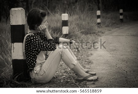 Sad young asian woman tourist hitchhiking along a road. wait for help