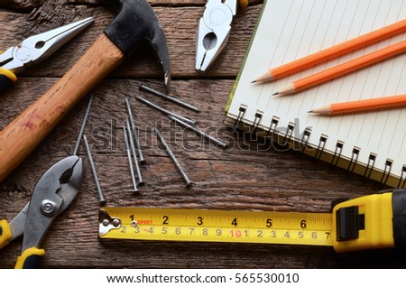  A top view image f a yellow tape measure and an open notebook on a wooden workbench.