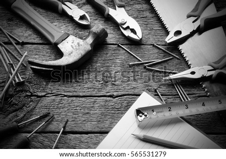 A black and white image of various hand tools and open notebook on a wooden workbench.