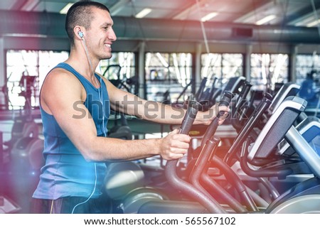 Smiling muscular man using elliptical machine at gym