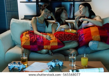 Three young women in living room, sitting on sofa Royalty-Free Stock Photo #565568077