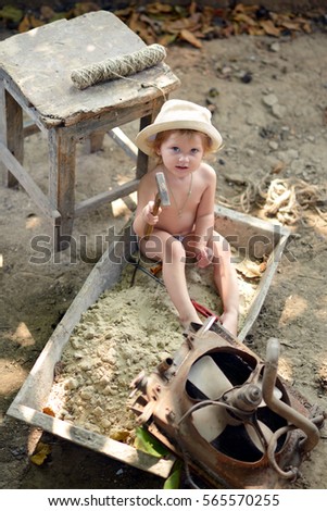 Nice baby. Father's daughter. Sweet girl in a hat sitting on the sand and playing with car parts.